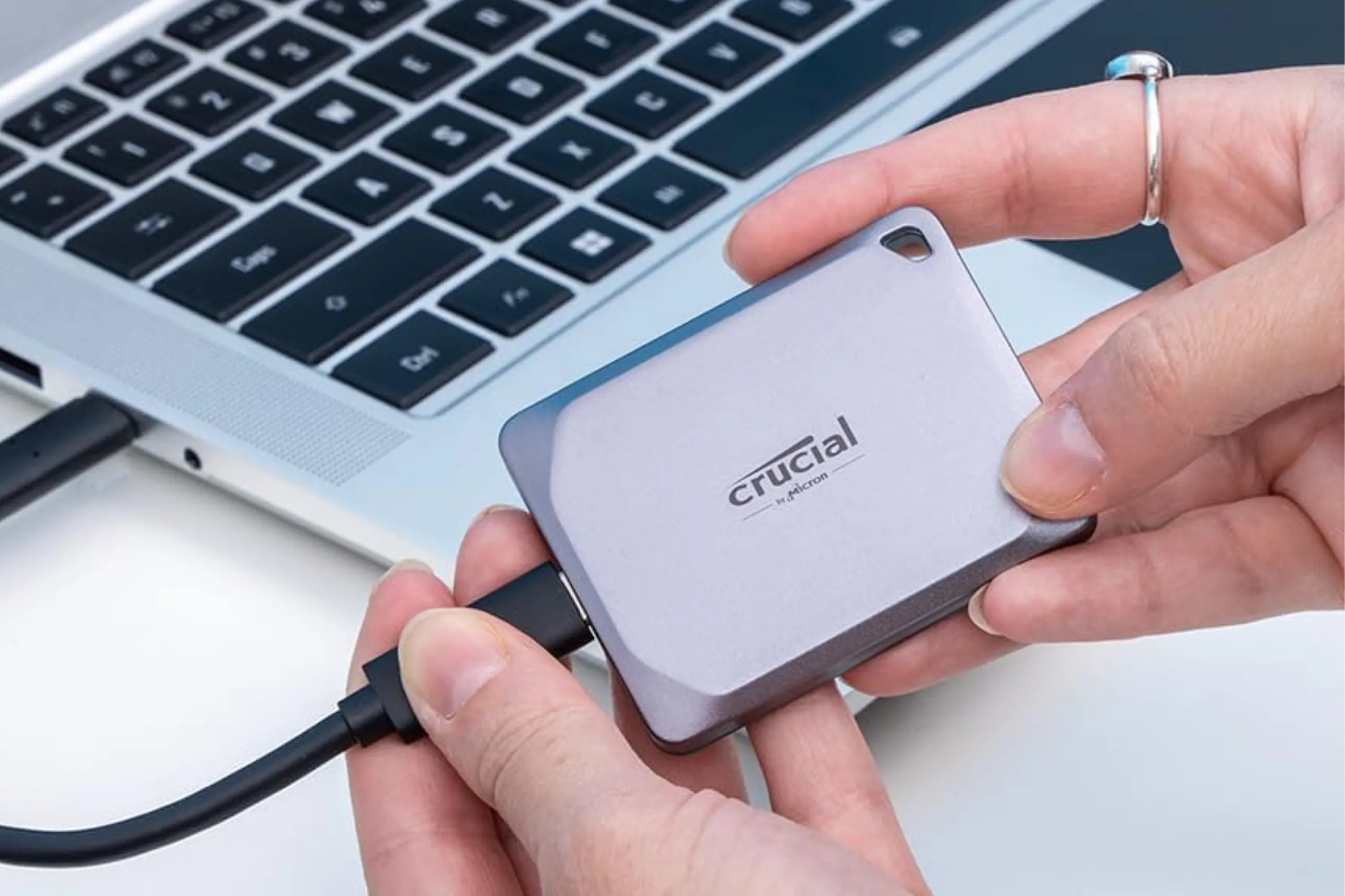 Người dùng cầm SSD Crucial X9 Pro 1TB cạnh máy tính, thể hiện tính di động và dễ sử dụng