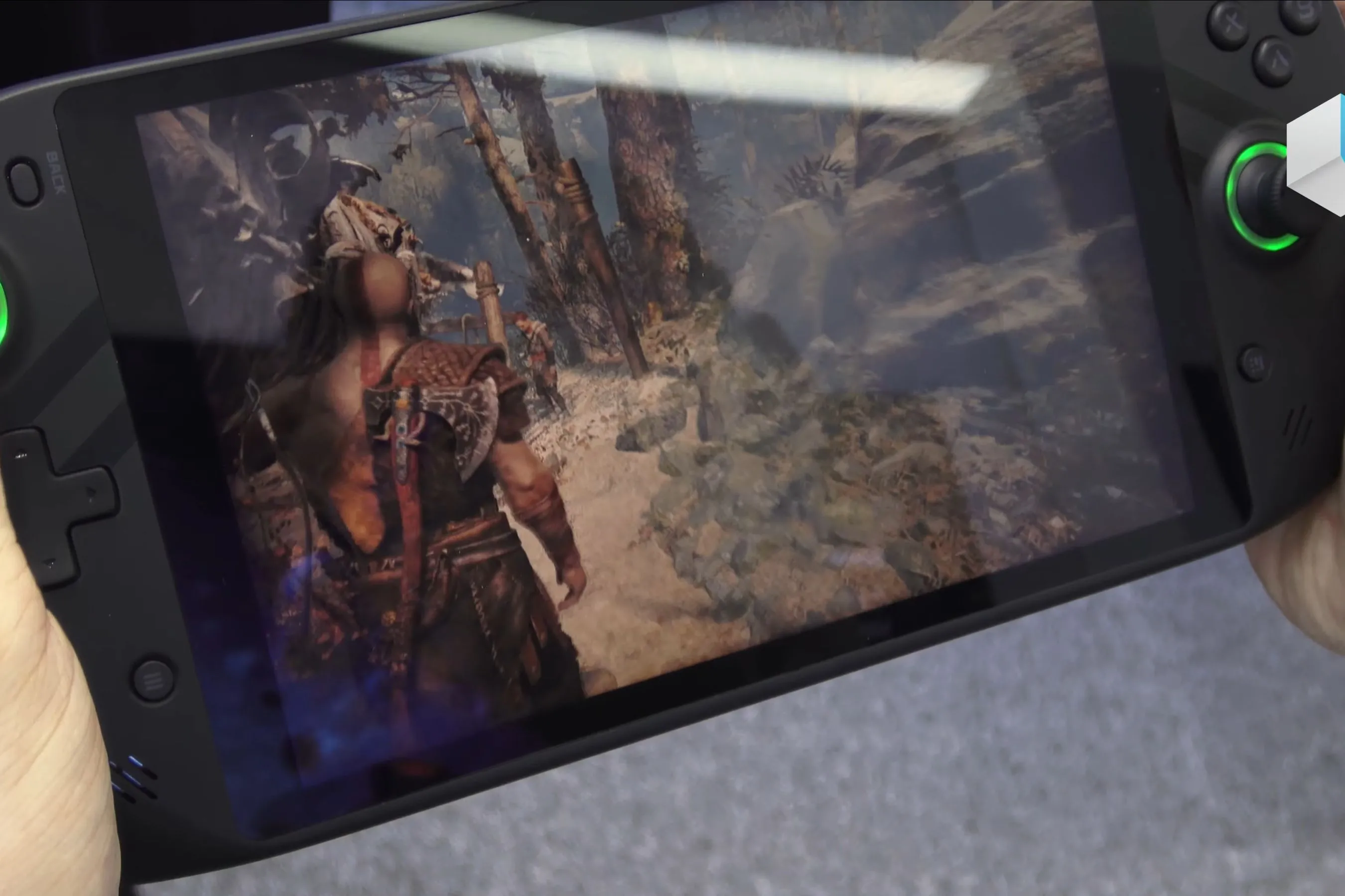 Thiết bị PC gaming handheld đang chạy game God of War, hiển thị nhân vật Kratos và Atreus.